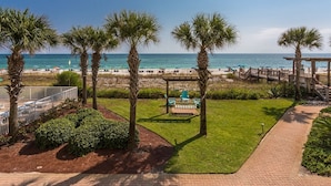 A view of a beachside patio with palm trees, a wooden deck, and a view of the ocean.