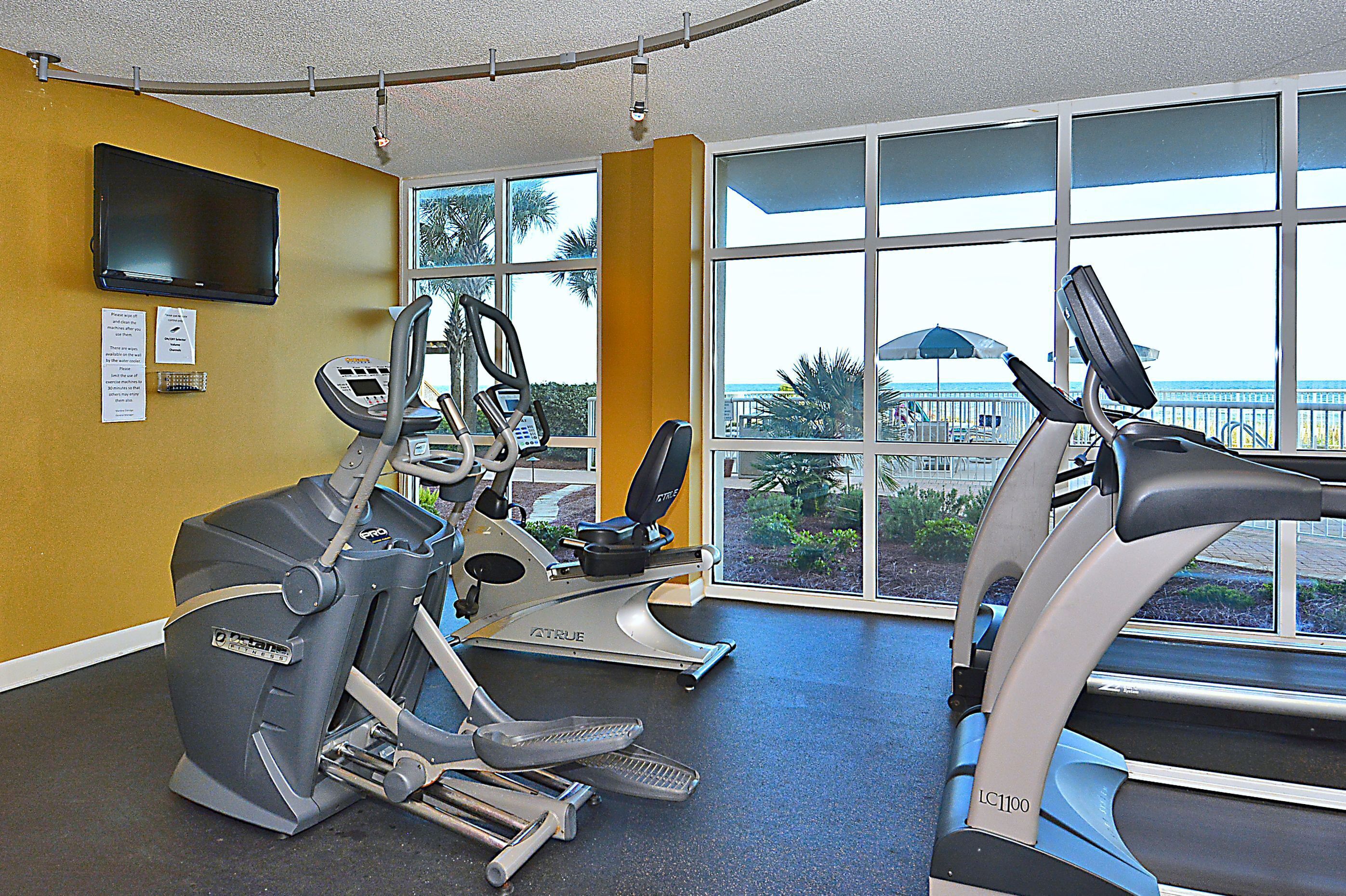 A gym with stationary bikes and treadmills, large windows with a view of the outdoors.