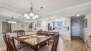 A spacious dining area with a wooden table and chairs, a chandelier, and a view of the kitchen and living area. - NEW LISTING! Sandy Key 515 5th floor -Beachfront view -NO HASSLE CHECK OUT (Pensacola)