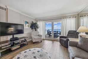 Relax in this stylish living room with a flat-screen TV, striped armchair, and sofa, offering a view of the sea from the balcony.