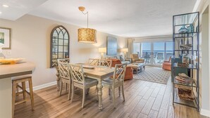 A spacious living area with a dining table, chairs, and a large window offering a view of the ocean. - Sandy Key 516 5th floor -Beachfront view -NO HASSLE CHECK OUT (Pensacola)