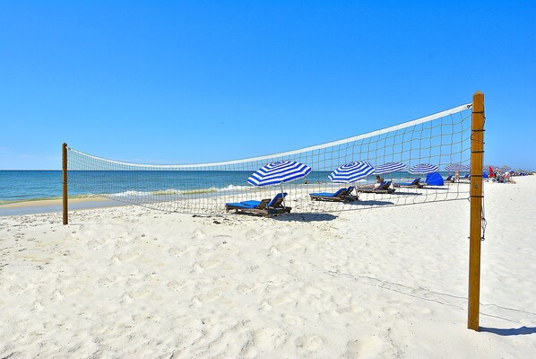 Enjoy a game of beach volleyball under the shade of striped umbrellas on the sandy beach.