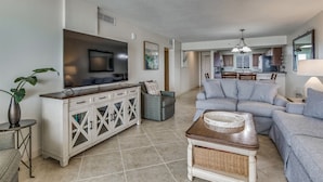 A spacious living room with a large TV, a sofa, and a dining area in the background.