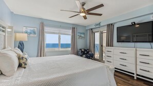A bedroom with a bed, a ceiling fan, a TV, a dresser, and a window with a view of the ocean. - Sandy Key 621 6th floor -Beachfront view -NO HASSLE CHECK OUT (Pensacola)