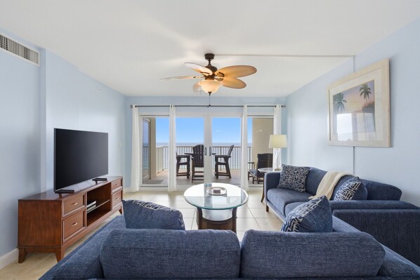 A living room with a TV, sofa, coffee table, and a ceiling fan. - Sandy Key 637 6th floor -Beachfront view -NO HASSLE CHECK OUT (Pensacola)