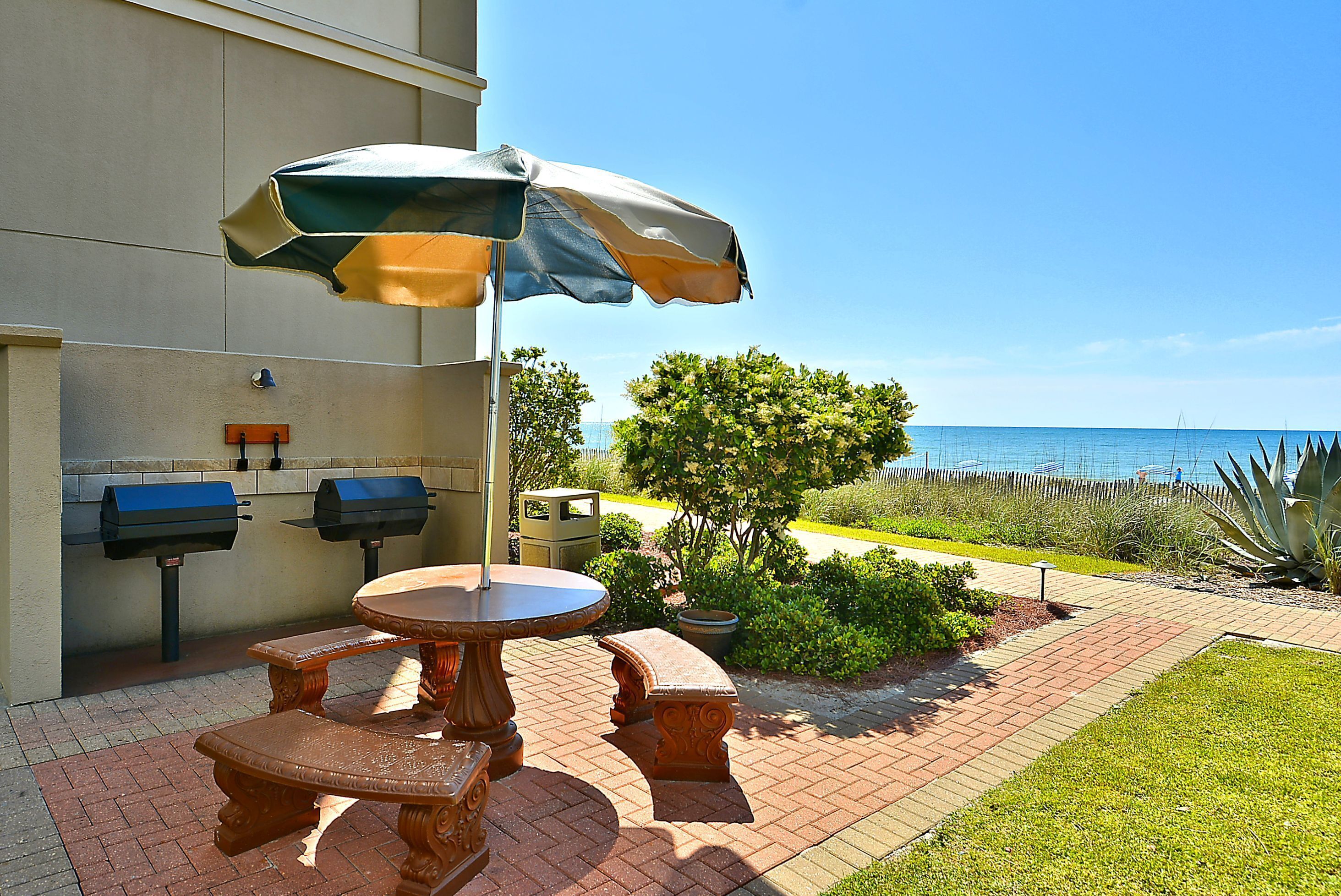Eine Terrasse im Freien mit Tisch, Bänken, Grill und Sonnenschirm.
