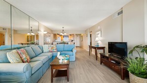 A modern living room with a sectional sofa, a coffee table, a TV stand, and a dining area in the background. - Sandy Key 735 -7th floor -Beachfront view -NO HASSLE CHECK OUT (Pensacola)