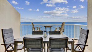 A balcony with a table and four chairs, overlooking a clear blue sky and ocean. - Sandy Key 812 -8th floor -Beachfront view -NO HASSLE CHECK OUT (Pensacola)