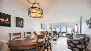 A spacious living room with a dining area, large windows offering a view, and a ceiling light fixture. - Sandy Key 812 -8th floor -Beachfront view -NO HASSLE CHECK OUT (Pensacola)