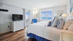 A hotel room with a bed, a TV on a white dresser, a chair, and a view of the ocean. - Sandy Key 812 -8th floor -Beachfront view -NO HASSLE CHECK OUT (Pensacola)