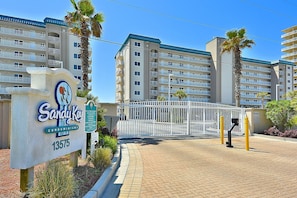 Une entrée fermée par un portail mène à un immeuble sur lequel est apposée une plaque indiquant « Sandy Key Condominiums 13575 ».
