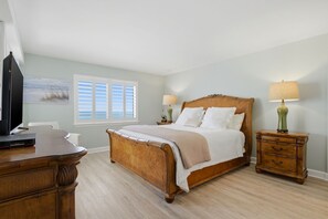 A bedroom with a wooden bed, a desk, a nightstand, and a window with shutters. - Sandy Key 818- 8th floor -Beachfront view -NO HASSLE CHECK OUT (Pensacola)