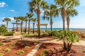 Ein Uferweg mit Palmen, einer Holzpergola und Blick auf das Meer.