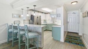 A modern kitchen with a central island, bar stools, pendant lighting, and a view into the dining area. - Sandy Key 8th floor -Beachfront view -NO HASSLE CHECK OUT (Pensacola)