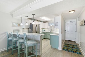A modern kitchen with a central island, bar stools, pendant lighting, and a view into the dining area. - Sandy Key 8th floor -Beachfront view -NO HASSLE CHECK OUT (Pensacola)