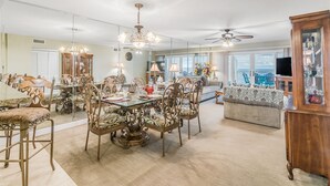 A spacious living area with a dining table, chairs, and a sofa. There is a ceiling fan and a television. - Sandy Key 826- 8th floor -Beachfront view -NO HASSLE CHECK OUT (Pensacola)