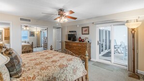 A bedroom with a bed, dresser, and a ceiling fan. There is a sliding glass door leading to a balcony with chairs. - Sandy Key 826- 8th floor -Beachfront view -NO HASSLE CHECK OUT (Pensacola)