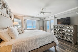 Quarto com cama, ventilador de teto, televisão e cómoda de madeira decorativa.