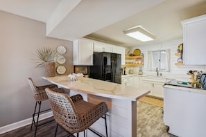 Een moderne keuken met witte kasten, een zwarte koelkast en een centraal eiland met barstoelen.