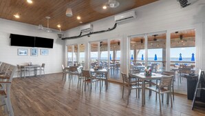 Un comedor amplio con suelo de madera, varias mesas y sillas, y ventanas grandes con vista al mar.