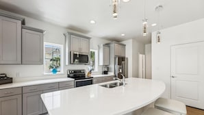 Una cocina moderna con armarios grises, una isla grande, electrodomésticos de acero inoxidable e iluminación colgante.