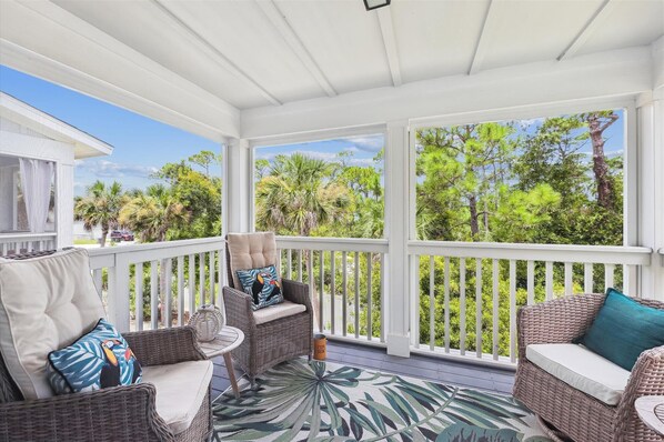 A covered porch with wicker furniture, a patterned rug, and a view of trees and sky.