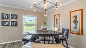 A dining area with a round table, black leather chairs, a chandelier, and framed artwork on the walls. - NEW LISTING! Lost Key Villas Golf & Beach Club ~Sea Salt - NO HASSLE CHECK OUT (Perdido Key)