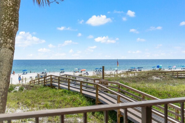 A beach with a wooden boardwalk leading to the shore, a flag, and beach umbrellas.