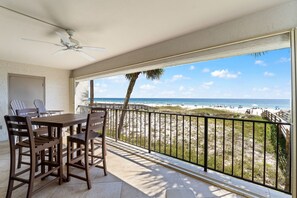 A balcony with a table and chairs, a ceiling fan, and a view of the beach.