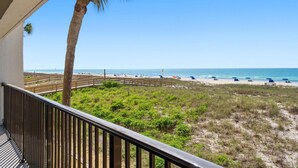 A balcony with a view of a beach, palm trees, and a wooden fence.