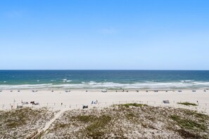 Une plage avec un rivage sablonneux, une clôture en bois et l’océan en arrière-plan.