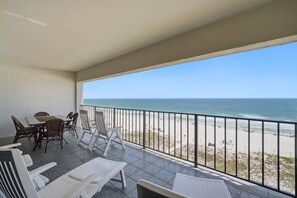 Un balcone con vista sulla spiaggia, un tavolo con sedie e alcuni lettini.
