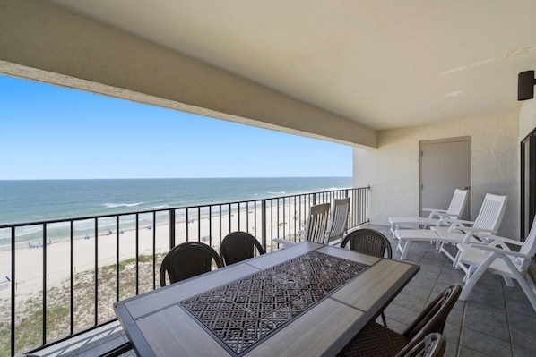 Een balkon met uitzicht op het strand, een tafel met stoelen en een deur.