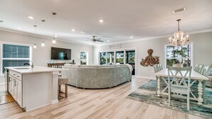A modern kitchen with a central island, a dining area with a white table and chairs, and a large window with blinds. - Lost Key Villas Golf & Beach Club ~Shore to Please - NO HASSLE CHECK OUT (Perdido Key)