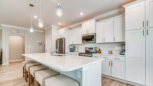 A modern kitchen with white cabinetry, a large island with bar stools, stainless steel appliances, and pendant lighting. - Lost Key Villas Golf & Beach Club ~Shore to Please - NO HASSLE CHECK OUT (Perdido Key)