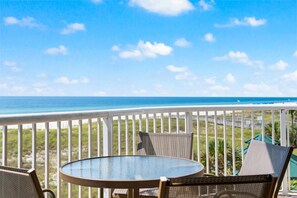 A balcony with a round table and two chairs, overlooking a beach and ocean.