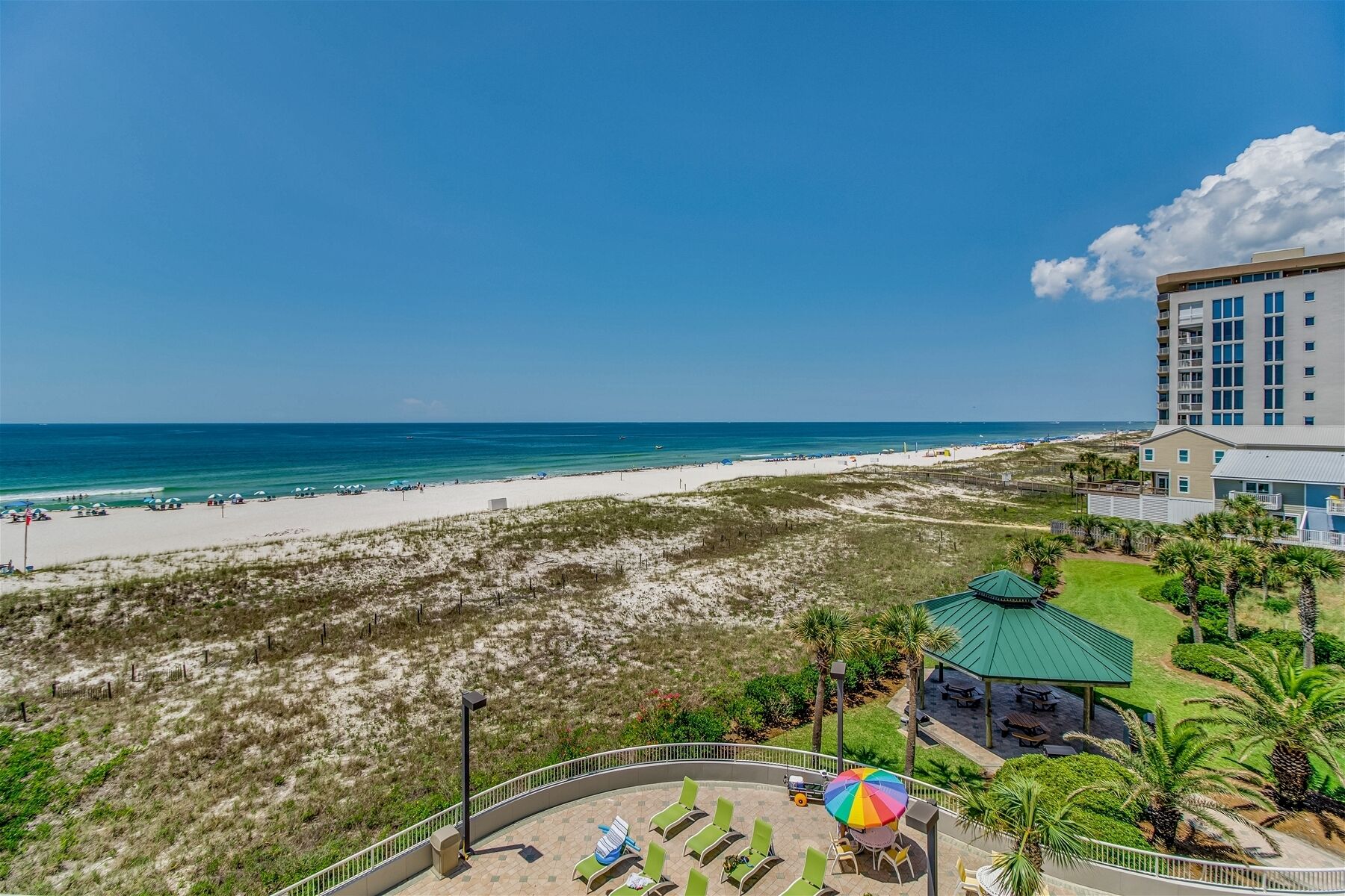 A beach view from a hotel balcony with a pool area, a beach, and a high-rise building in the background.