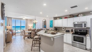 A modern kitchen with white cabinets, a central island, stainless steel appliances, and a view of the ocean. - Spanish Key 207  Beachfront view  - NO HASSLE CHECK OUT (Perdido Key)