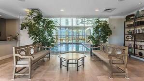 A spacious indoor area with a large window overlooking a pool, two wooden benches, and a small table. - Spanish Key 207  Beachfront view  - NO HASSLE CHECK OUT (Perdido Key)