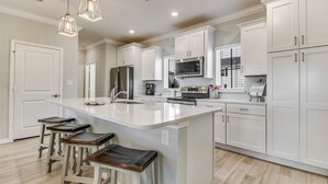 A modern kitchen with white cabinetry, a large island with stools, stainless steel appliances, and pendant lighting.
