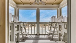 A covered porch with white railings and benches, offering a view of the beach and city skyline.