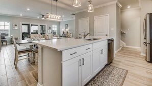 A modern kitchen with a large island, white cabinetry, and pendant lighting.