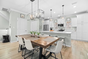 Una cocina moderna con armarios blancos, una mesa de comedor de madera e iluminación colgante.