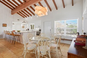 A spacious kitchen with white cabinetry, a central island, and a dining area with a round glass table and wicker chairs.