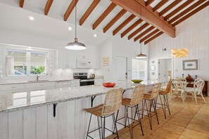 Una cocina con una isla grande, taburetes de bar e iluminación colgante.