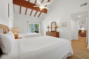 A bedroom with two beds, wooden beams, a ceiling fan, and a view of the outdoors.