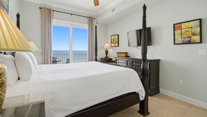 A bedroom with a bed, a ceiling fan, a window with curtains, a dresser, and artwork on the wall.