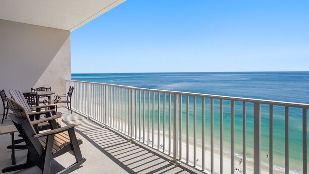 A balcony with a view of the ocean, a table, and two chairs.