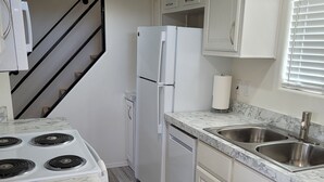 Una cocina con armarios blancos, un refrigerador blanco, una estufa y un lavamanos.