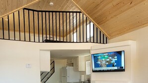 Un área de estar amplia con techo alto, chimenea, televisor y escalera que sube a un nivel superior.